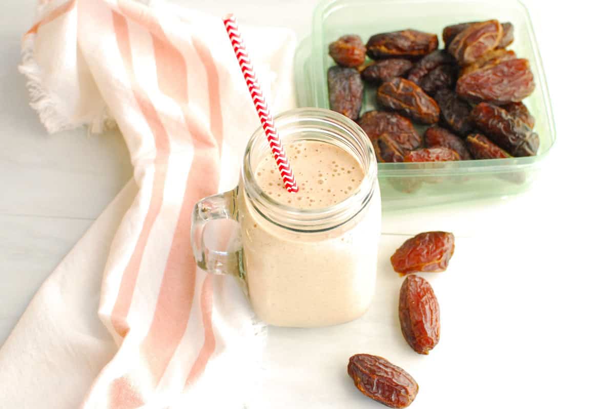 A mason jar filled with a cinnamon date smoothie, next to some dates and a napkin.