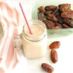 A mason jar filled with a cinnamon roll date smoothie, next to some fresh dates and a napkin.
