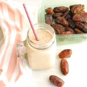 A mason jar filled with a cinnamon roll date smoothie, next to some fresh dates and a napkin.