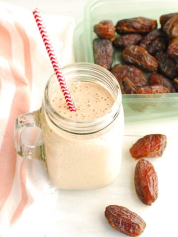 A mason jar filled with a cinnamon roll date smoothie, next to some fresh dates and a napkin.