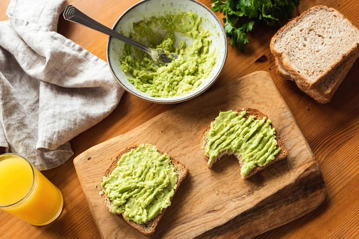 Two pieces of avocado toast on a wooden cutting board.
