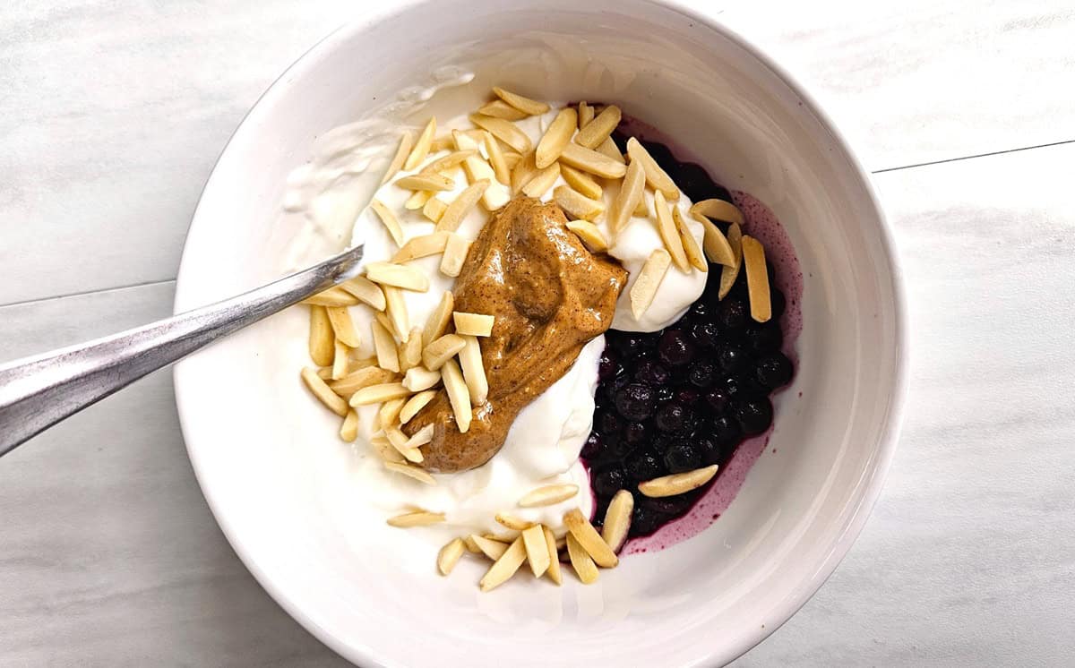 A bowl of yogurt with wild blueberries, almond butter, and almonds.