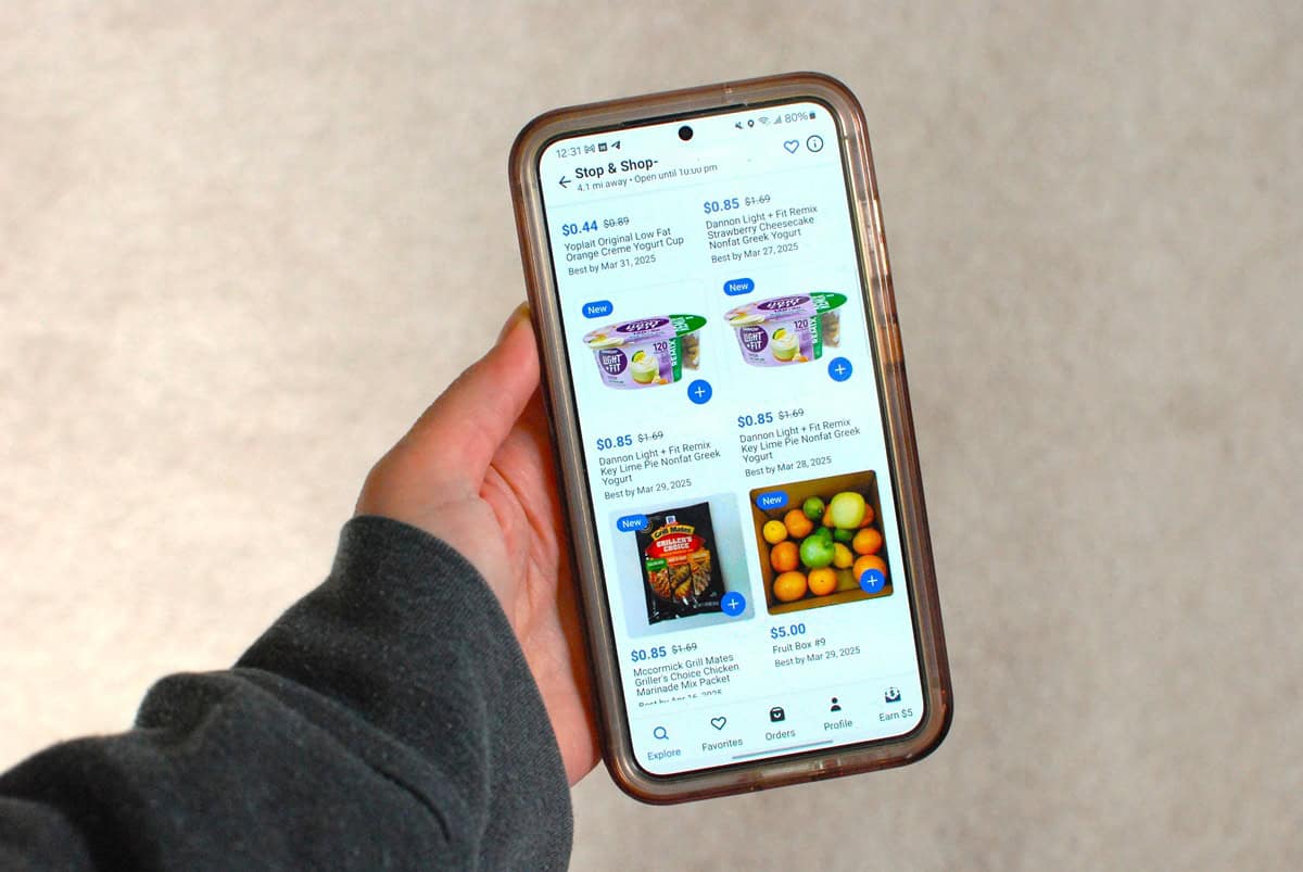 A woman's hand holding a phone displaying the Flashfood app options at one store.