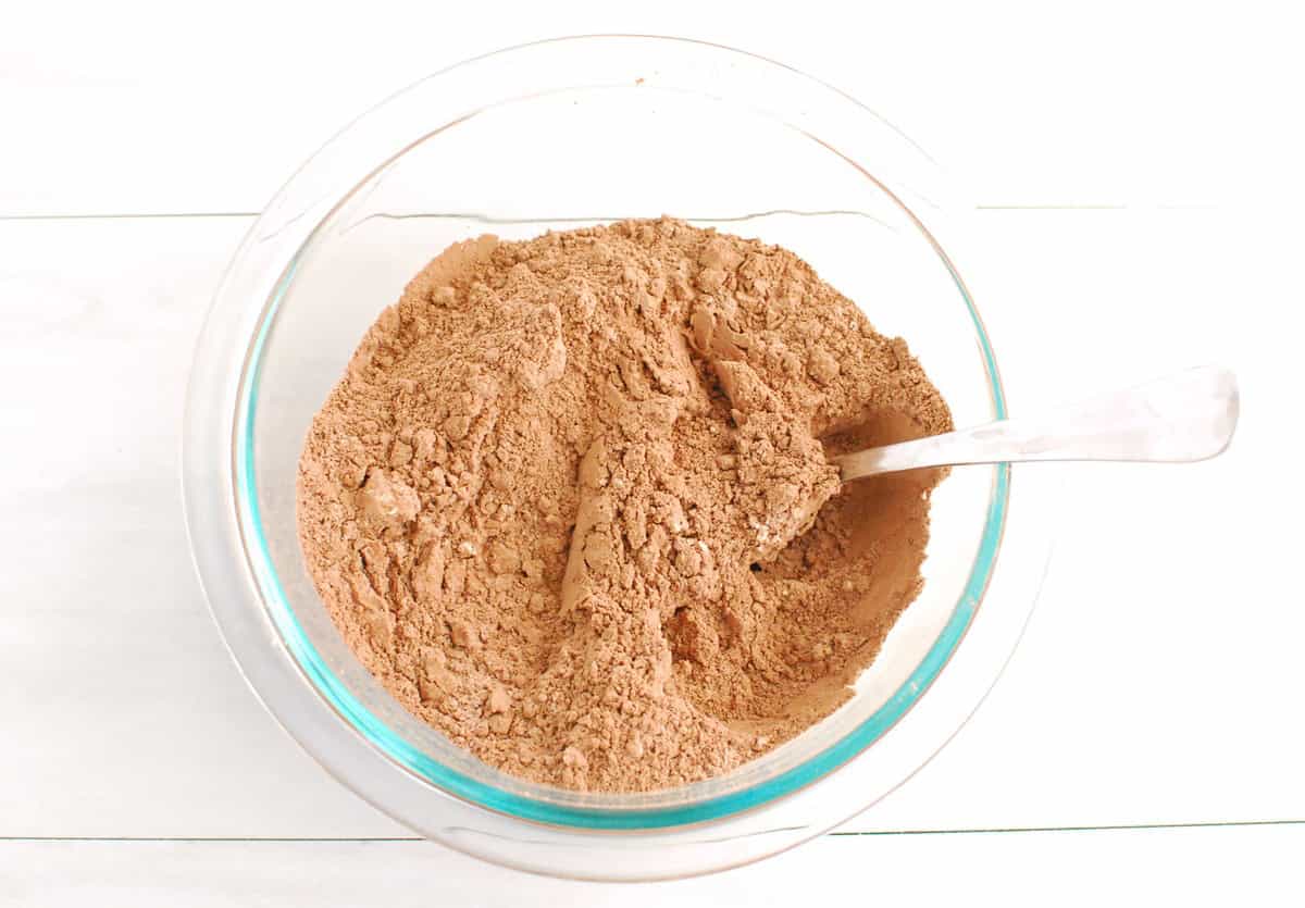 Cocoa powder, flour, protein powder, baking powder, and salt mixed together in a glass bowl.