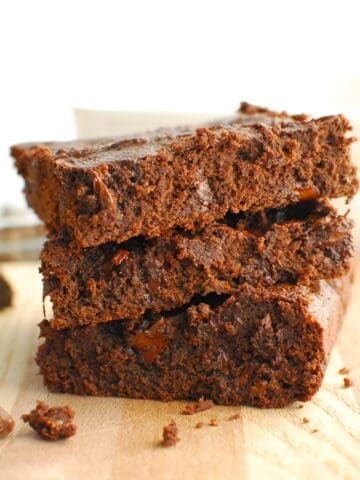A stack of three cottage cheese brownies on a wooden cutting board.