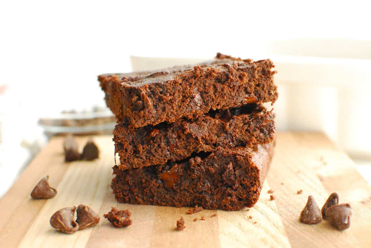 A stack of three cottage cheese brownies on a wooden cutting board.