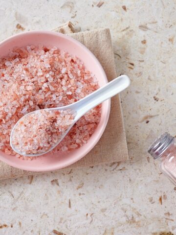 Pink salt in a pink bowl next to a salt shaker.