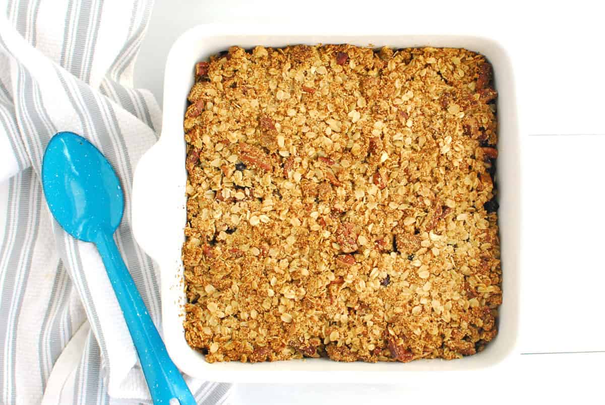 A baking dish full of blueberry sweetpotato crisp, next to a serving spoon.