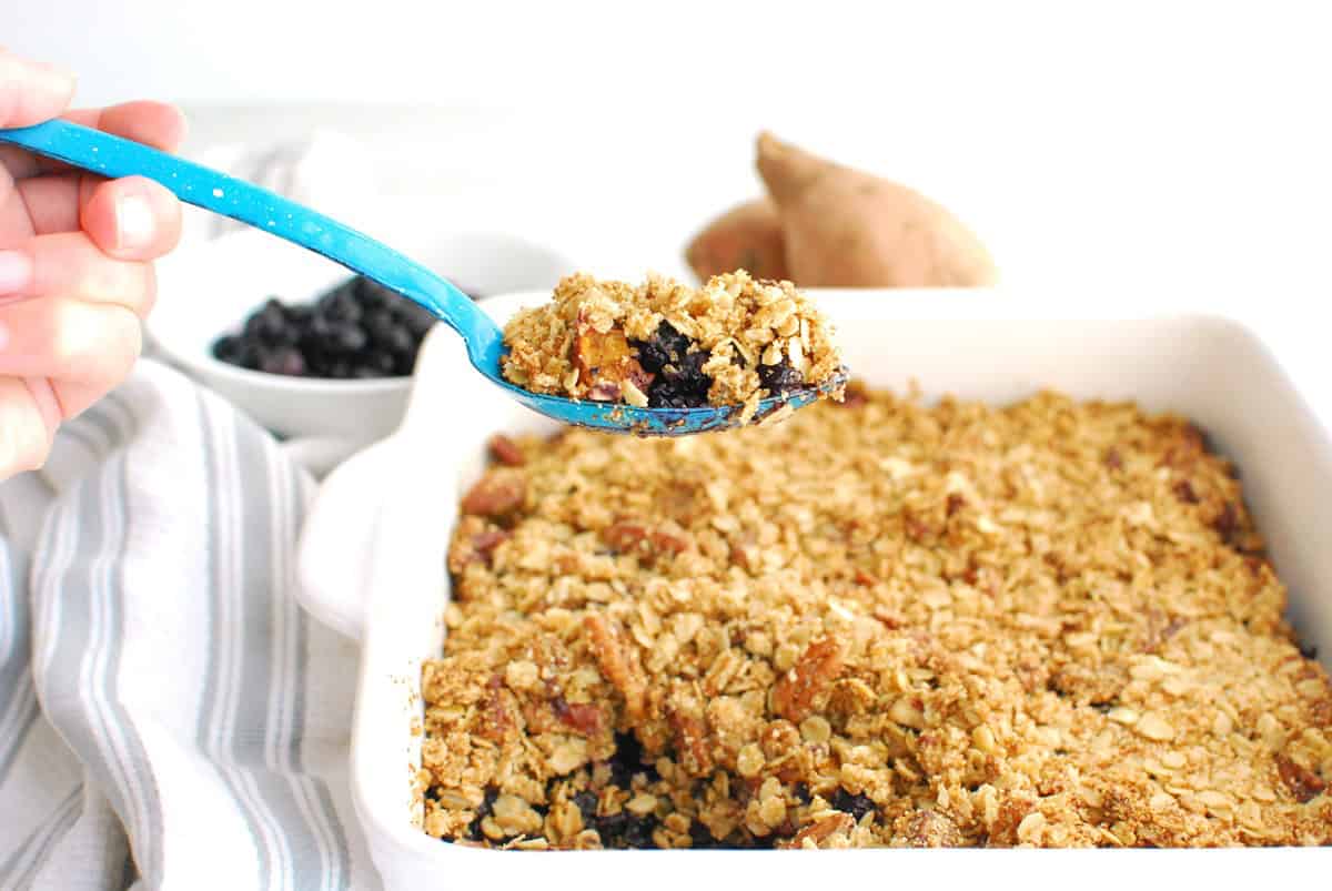 A serving spoon scooping out sweetpotato blueberry crisp.