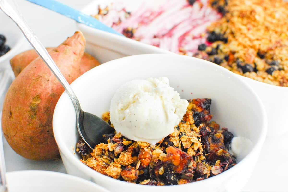 A bowl of sweetpotato blueberry crisp topped with oat milk ice cream.