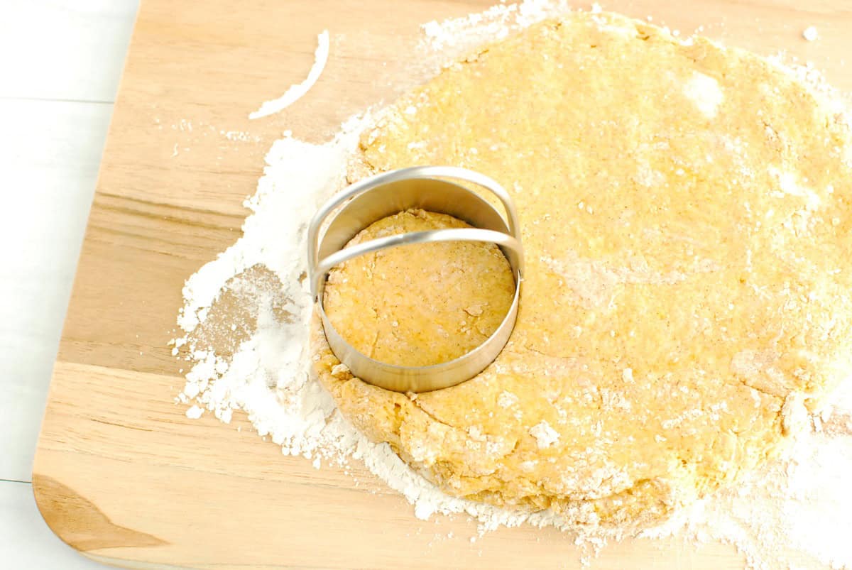 Sweetpotato biscuit dough patted into a disc on a floured surface, with a biscuit cutter cutting out dough.