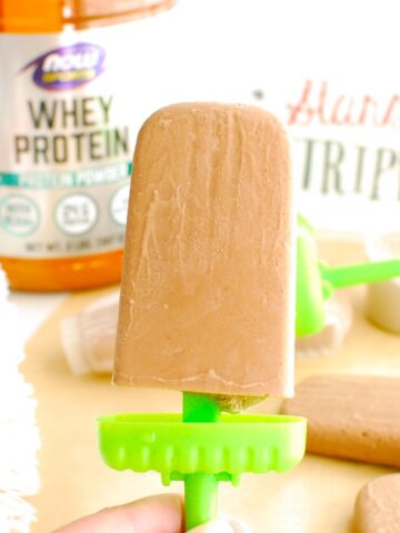 A woman's hand holding a chocolate peanut butter protein popsicle.