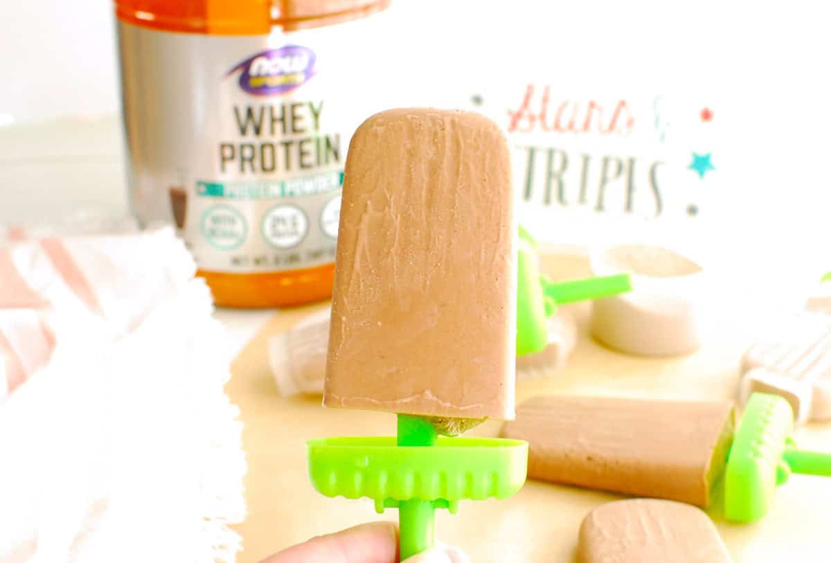 A woman's hand holding a chocolate peanut butter protein popsicle.