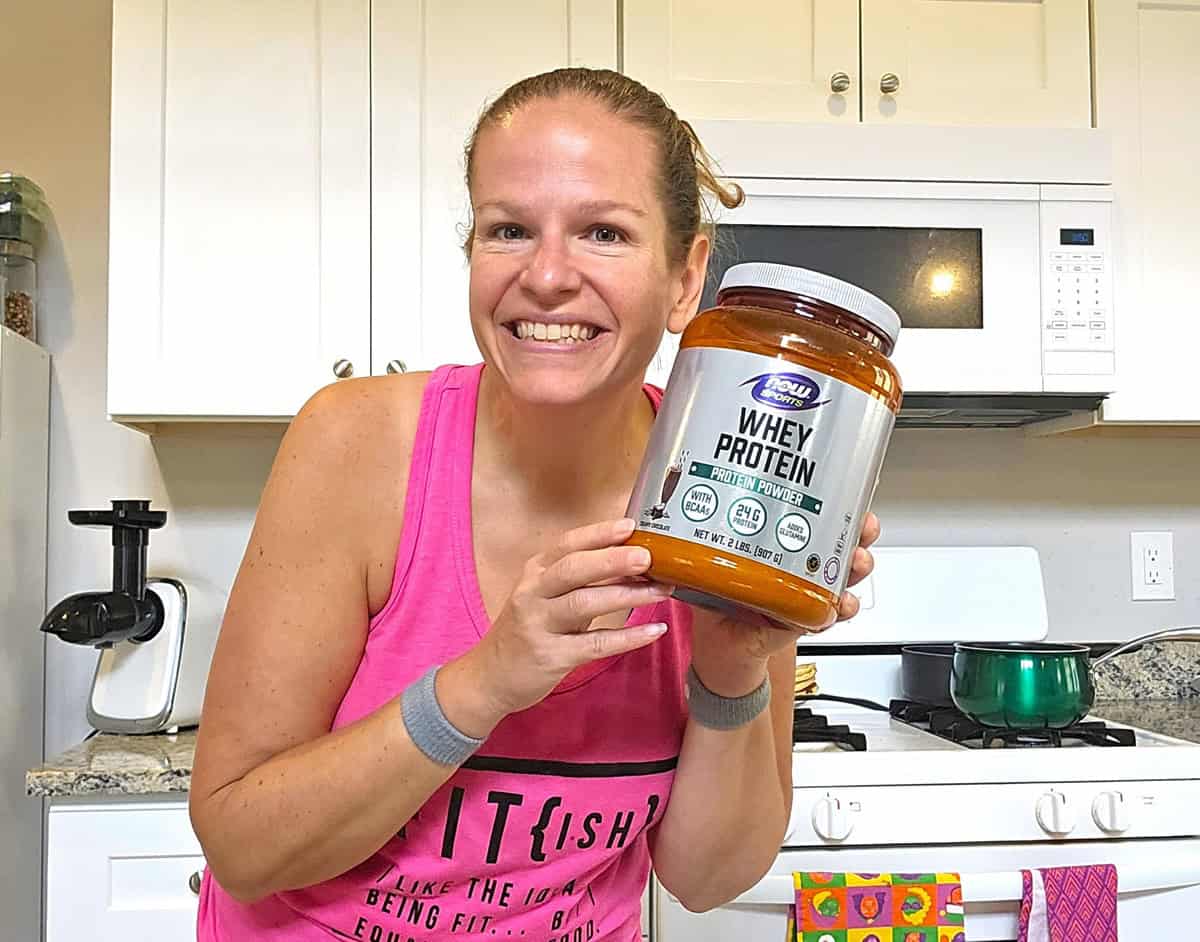 A woman holding a container of chocolate whey protein powder.