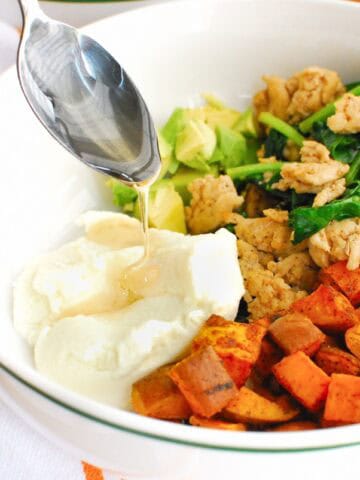 A spoon drizzling honey on ricotta in a sweetpotato breakfast bowl.