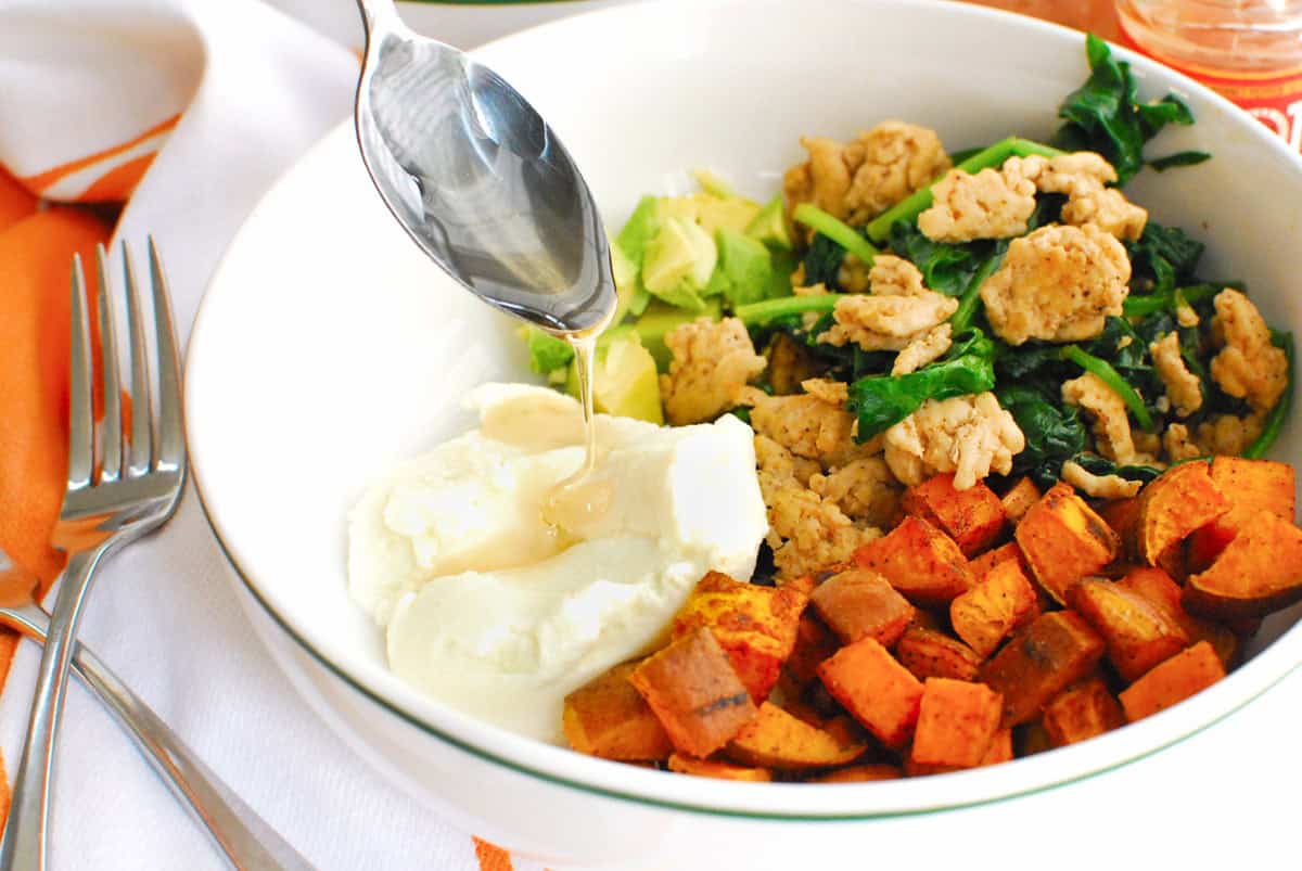 A spoon drizzling honey on ricotta in a sweetpotato breakfast bowl.