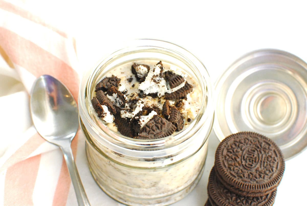A jar of oreo overnight oats next to a spoon and a few oreos.