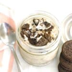 A jar filled with oreo overnight oats next to a napkin, spoon, and a few extra oreos.