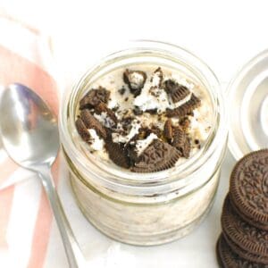 A jar filled with oreo overnight oats next to a napkin, spoon, and a few extra oreos.
