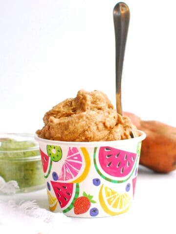 A cup full of strawberry sweetpotato nice cream with a spoon stuck into it.