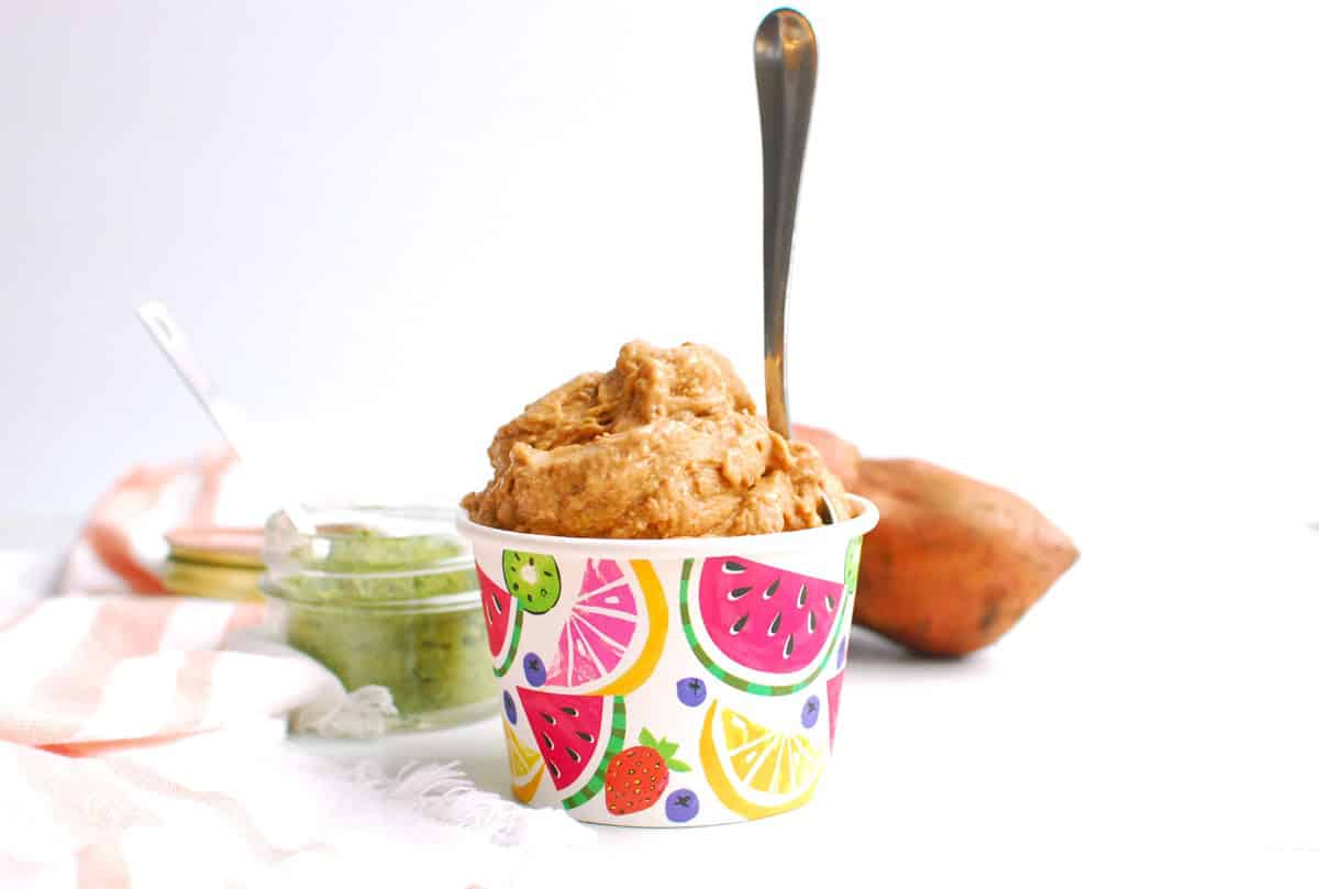 A cup full of strawberry sweetpotato nice cream with a spoon stuck into it.