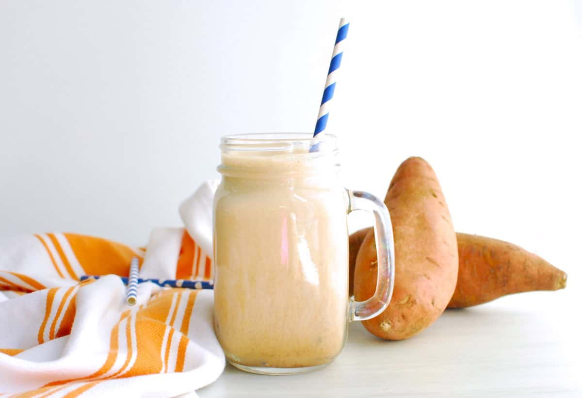 A high protein iced sweetpotato latte next to a napkin and fresh sweetpotatoes.