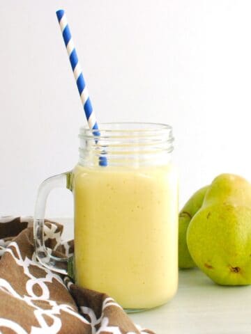 A mango pear smoothie in a glass next to fresh pears.