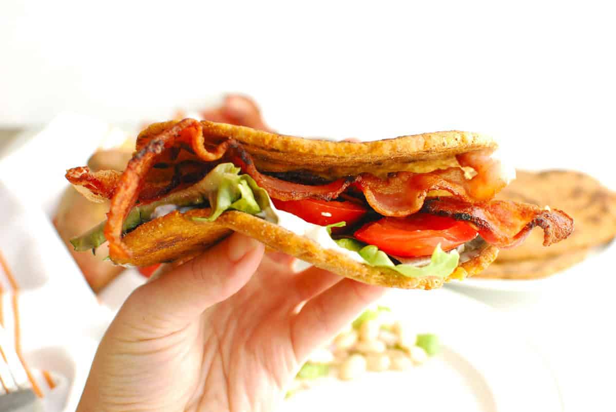 A woman's hand holding a sweetpotato flatbread BLT.