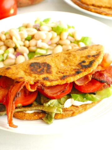 A sweetpotato flatbread BLT sandwich on a plate next to a bean salad.