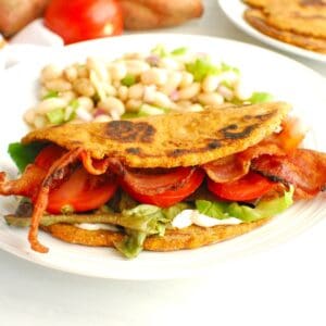 A sweetpotato flatbread BLT next to a bean salad on a white plate.