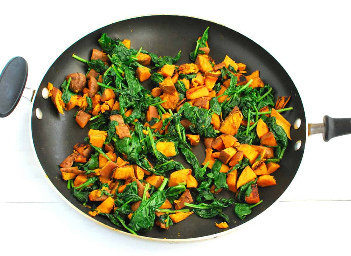 Sweetpotatoes and spinach sauteed in a skillet.