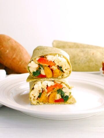 Two halves of a Mediterranean breakfast burrito on a plate.