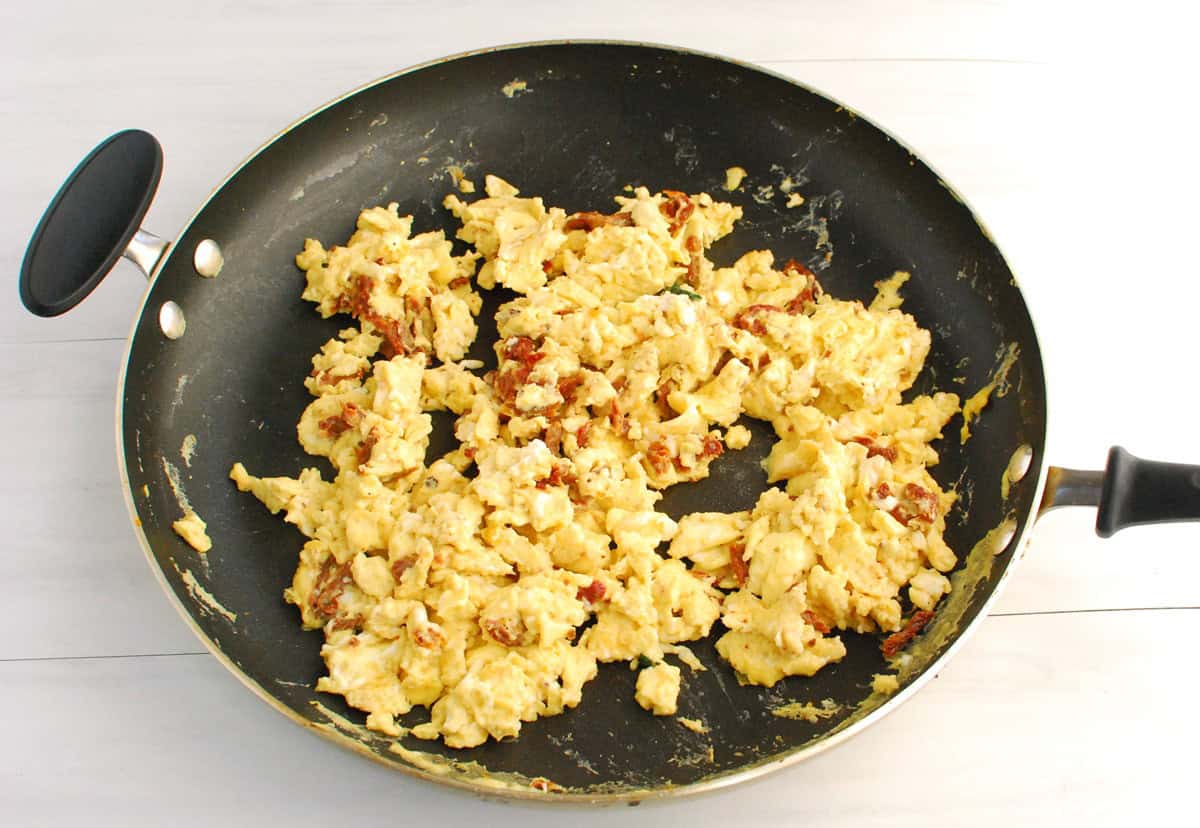 Scrambled eggs with sun-dried tomatoes in a skillet.