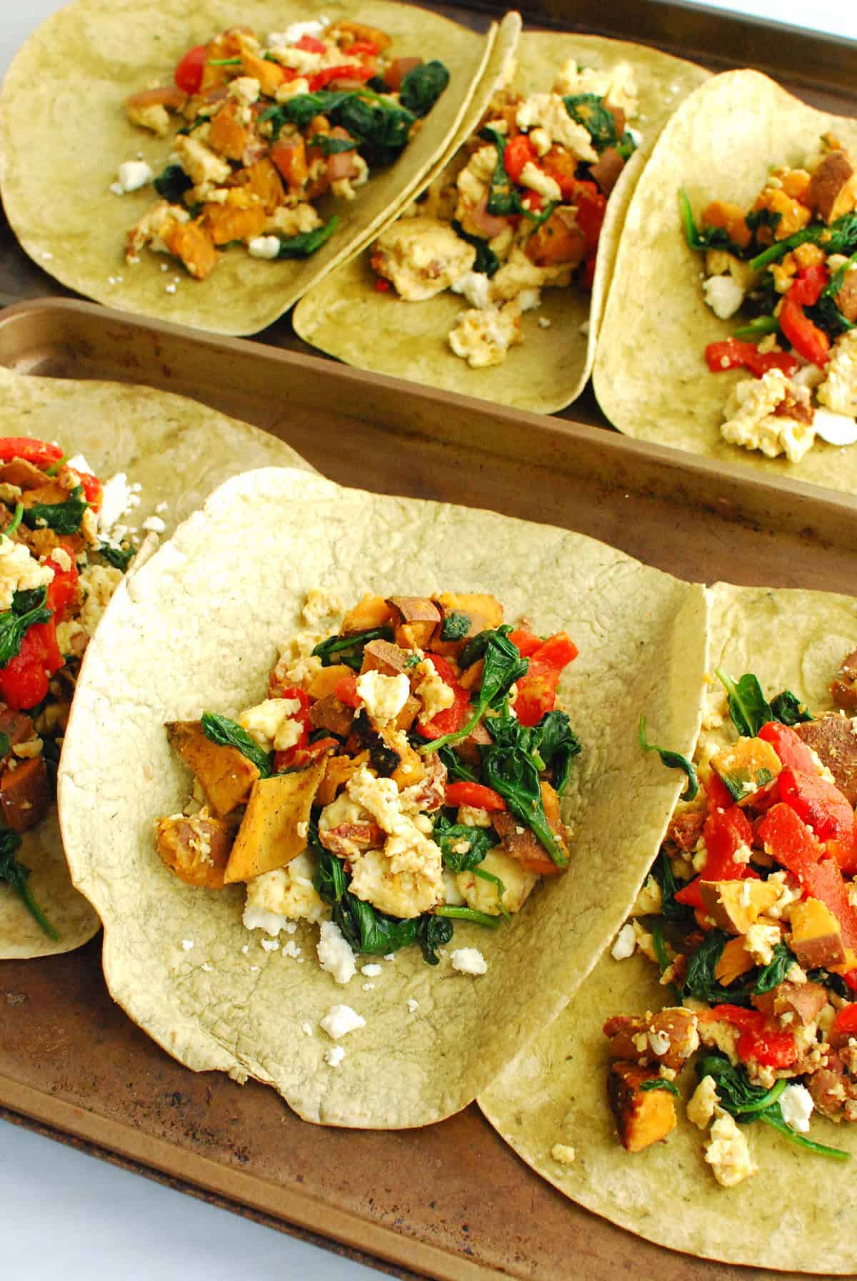 Wraps laid out on baking sheets and filled with breakfast burrito filling.