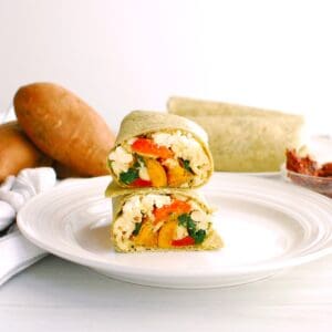 A mediterranean breakfast burrito that's been cut in half showing the filling with eggs, sweetpotatoes, roasted red peppers, sun dried tomato, and feta.