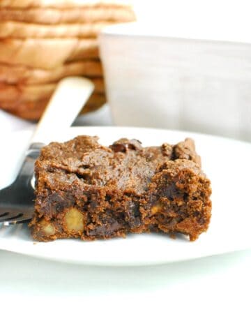 A pumpkin protein brownie on a white plate with a fork next to it.