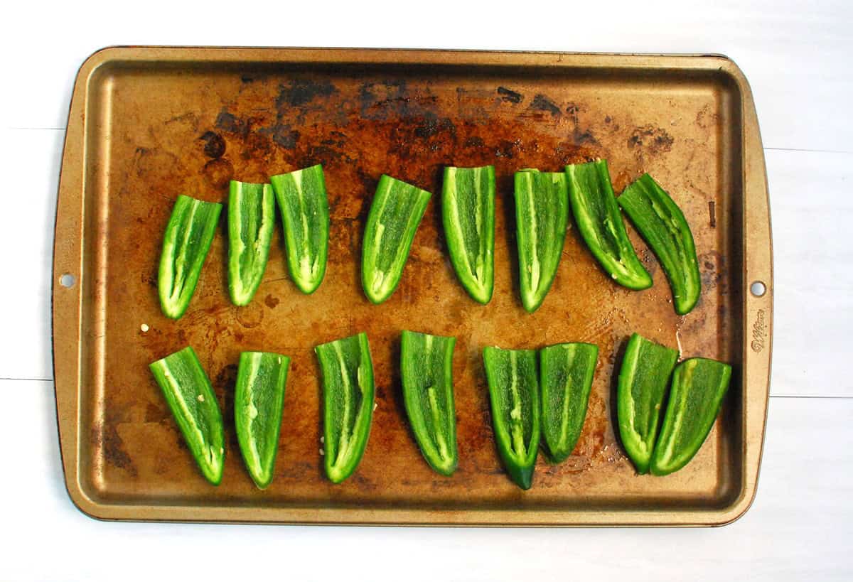 Jalapenos sliced in half on a baking sheet.