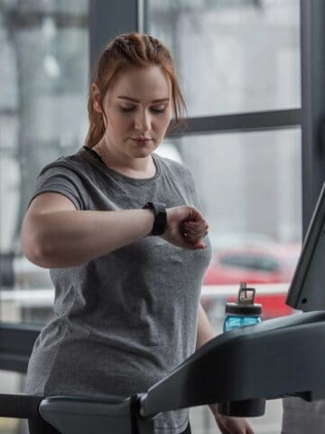 A woman looking at her watch on the treadmill, about to begin a HIIT workout.