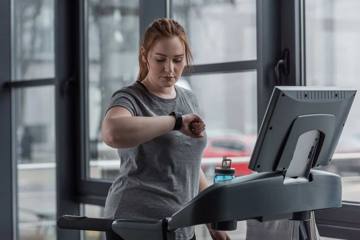 A woman looking at her watch on the treadmill, about to begin a HIIT workout.