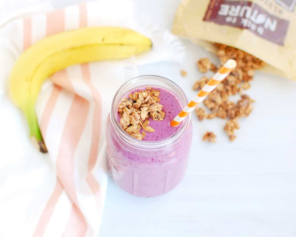A berry banana granola smoothie with a banana and granola in the background.