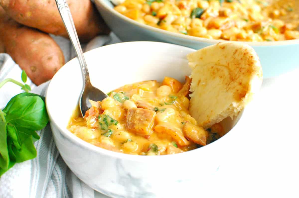 A white bowl filled with creamy beans and sweetpotatoes and a side of flatbread.