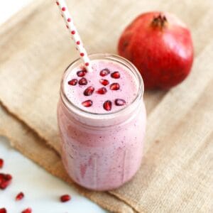 A mason jar filled with cranberry pomegranate smoothie garnished with pomegranate arils.