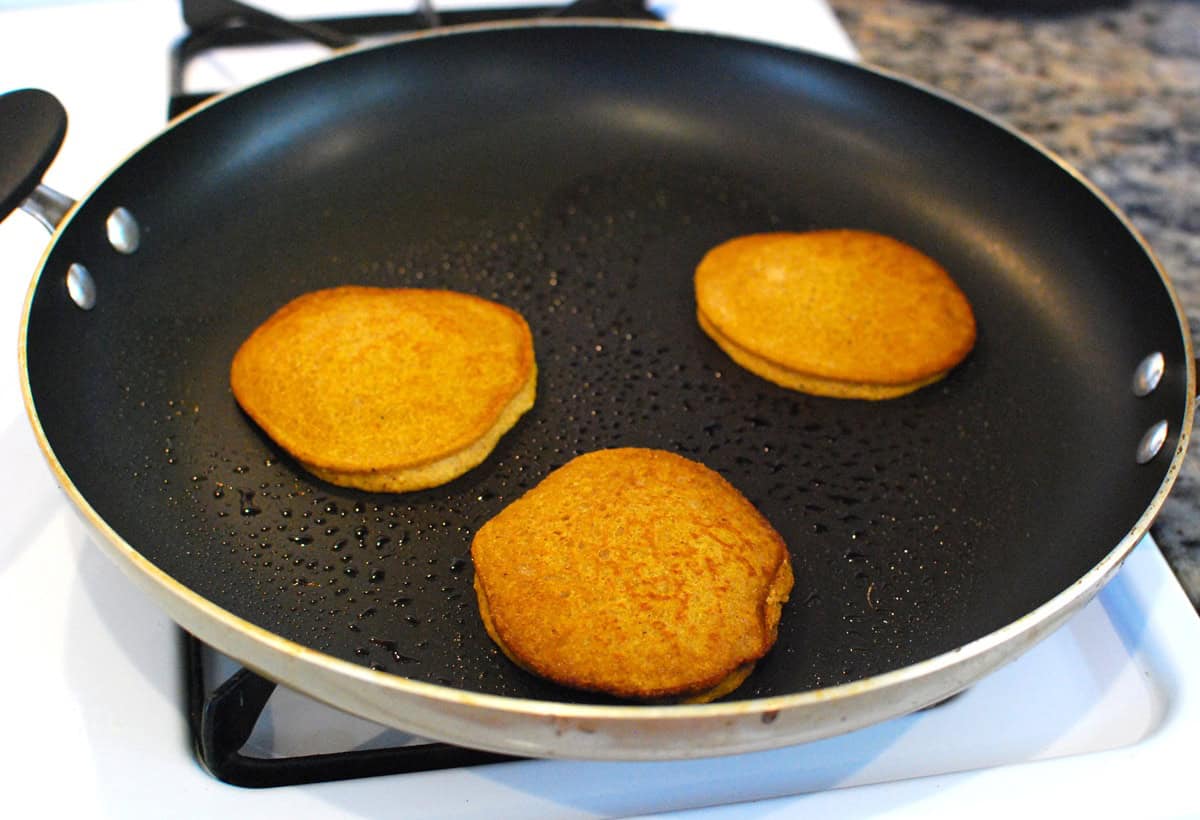 A small batch of gingerbread pancakes being cooked in a large skillet.