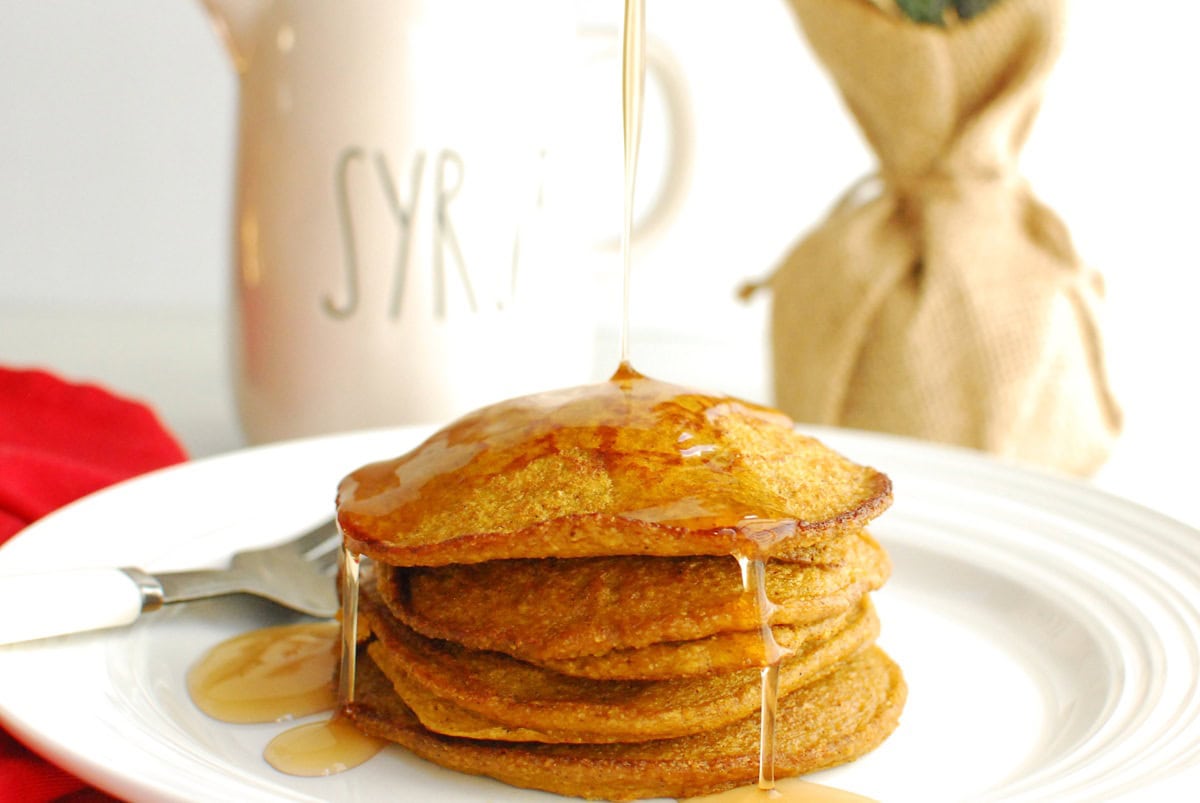 Gingerbread pumpkin pancakes with syrup being drizzled over the top.