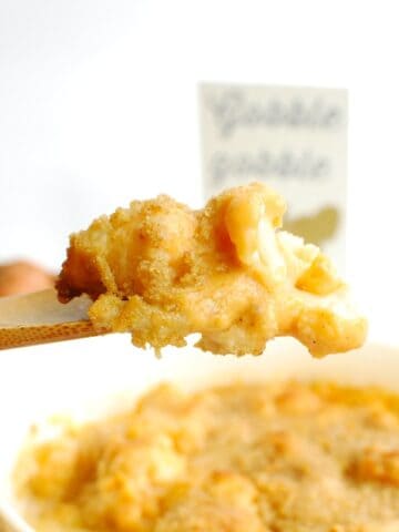 A wooden spoon scooping out a serving of sweetpotato cauliflower gratin.