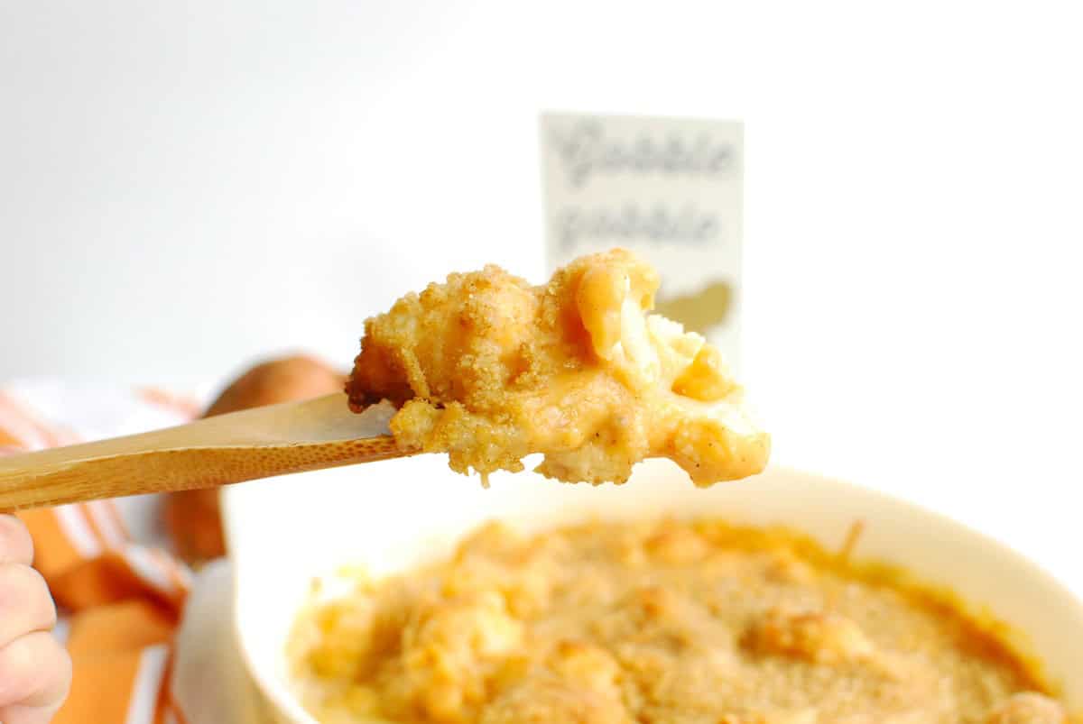 A wooden spoon scooping out a serving of sweetpotato cauliflower gratin.