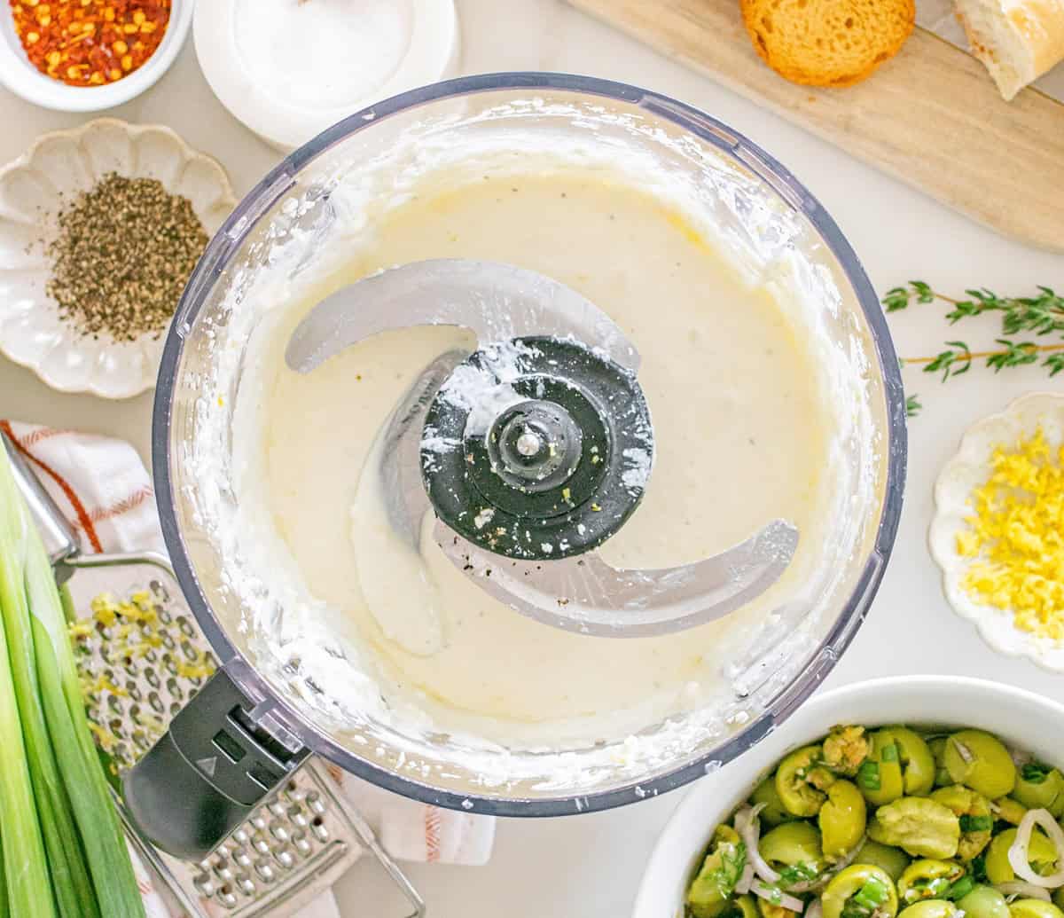 A food processor bowl that has whipped feta, yogurt, olive oil, lemon zest, and seasonings together.