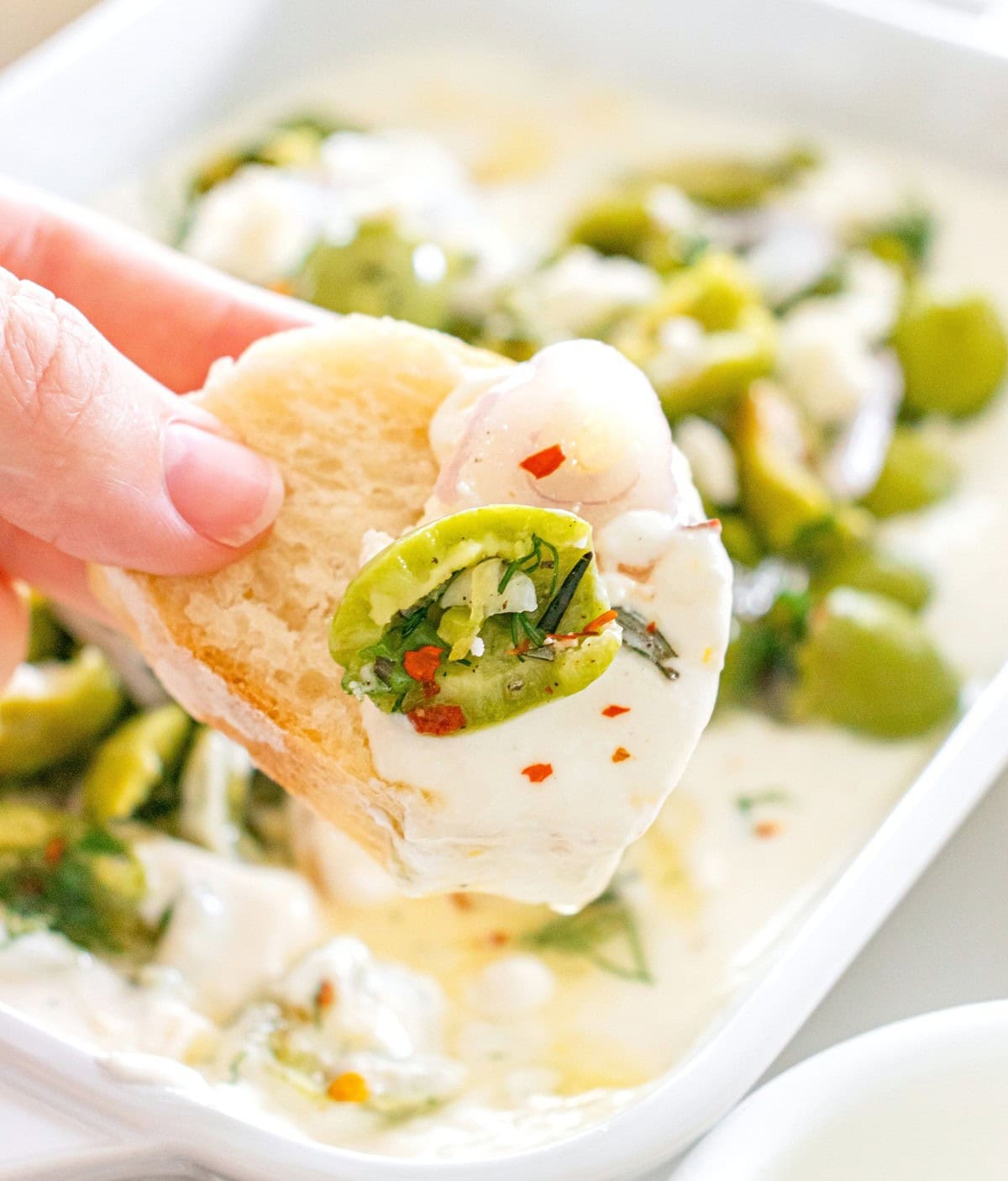 A woman's hand holding a crostini topped with feta yogurt dip.