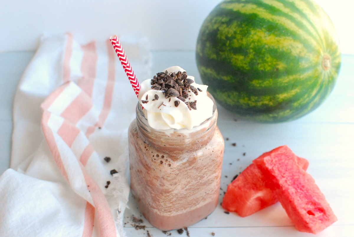 A glass of watermelon hot chocolate garnished with whipped cream and extra chocolate shavings.