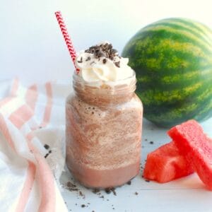 A glass mason jar mug filled with watermelon frozen hot chocolate with a red straw in the glass.